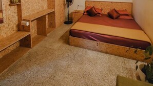 Une pièce avec un lit, des étagères en bois, un ventilateur et une petite plante.