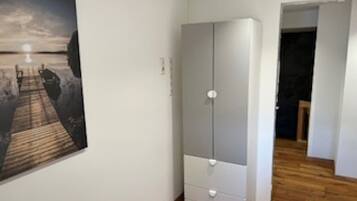 A bedroom with a wooden floor, a white wardrobe, and a painting on the wall.