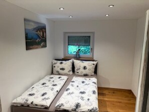 A small room with two beds, a window with blinds, a painting on the wall, and a wooden floor. - Holiday Home 'Ferienhaus 6 Personen' with Private Terrace, Private Garden and Wi-Fi (Weißensberg)