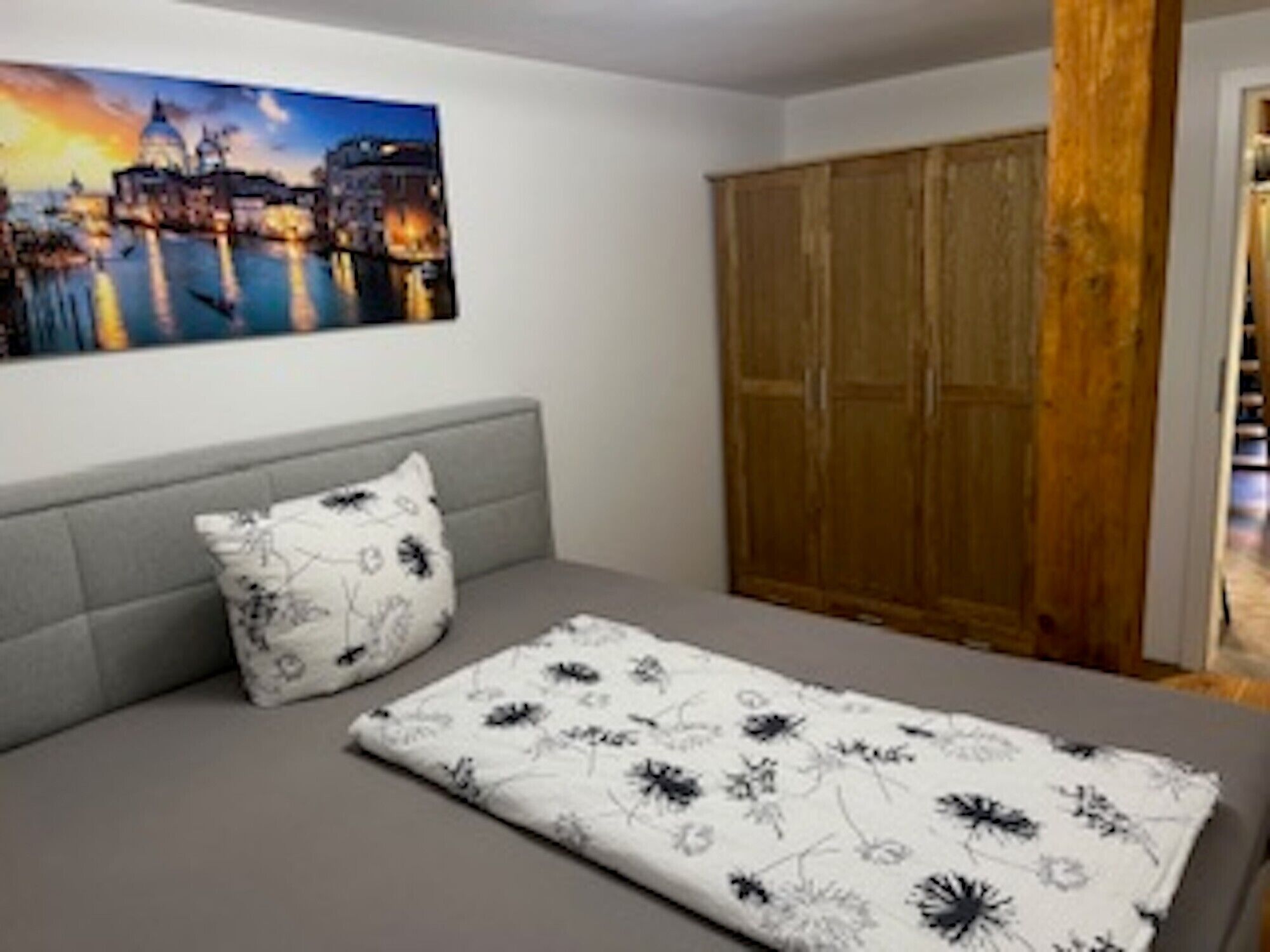 Ein Schlafzimmer mit einem Bett, einem grauen Sofa, einem Holzschrank und einem Stadtbild.