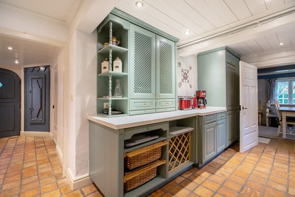 A kitchen with a built-in cabinet, a coffee maker, and a tiled floor.