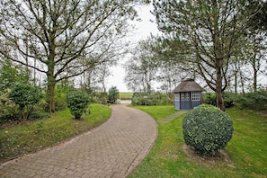 A paved pathway leading to a small blue building surrounded by trees and greenery.