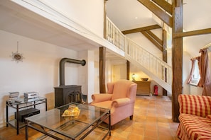 A spacious living area with a fireplace, a glass coffee table, a striped armchair, and a staircase with wooden beams.