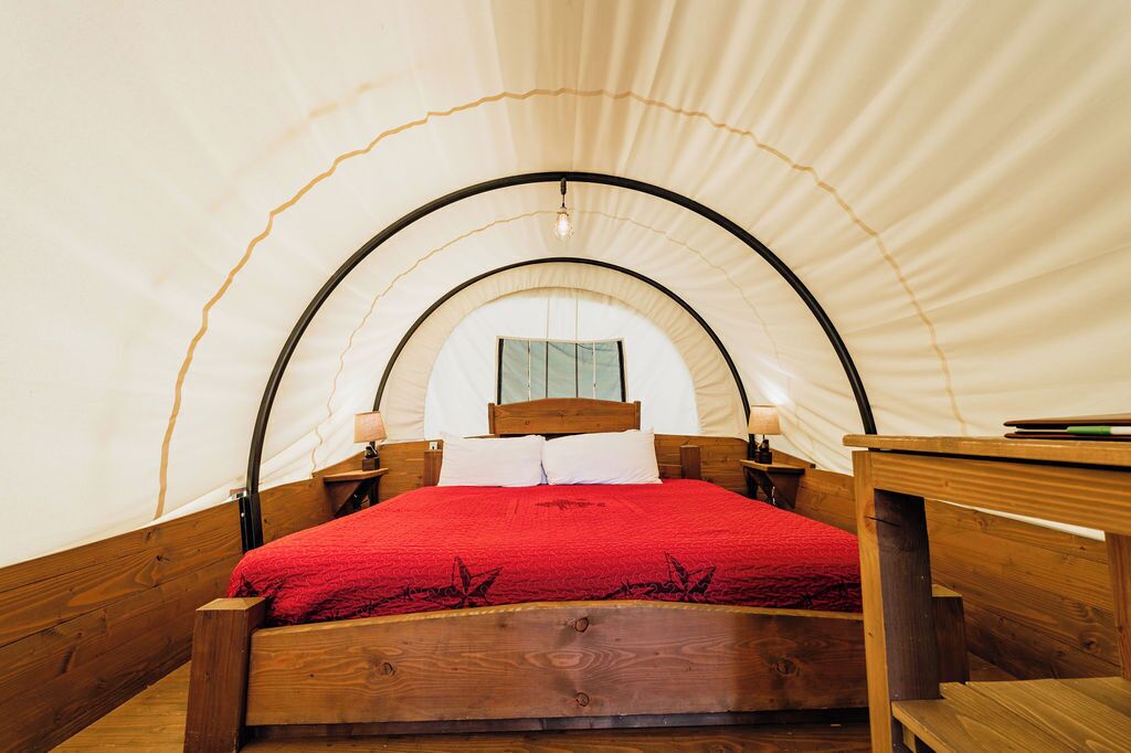 A tent with a wooden bed, a small table, and a window.