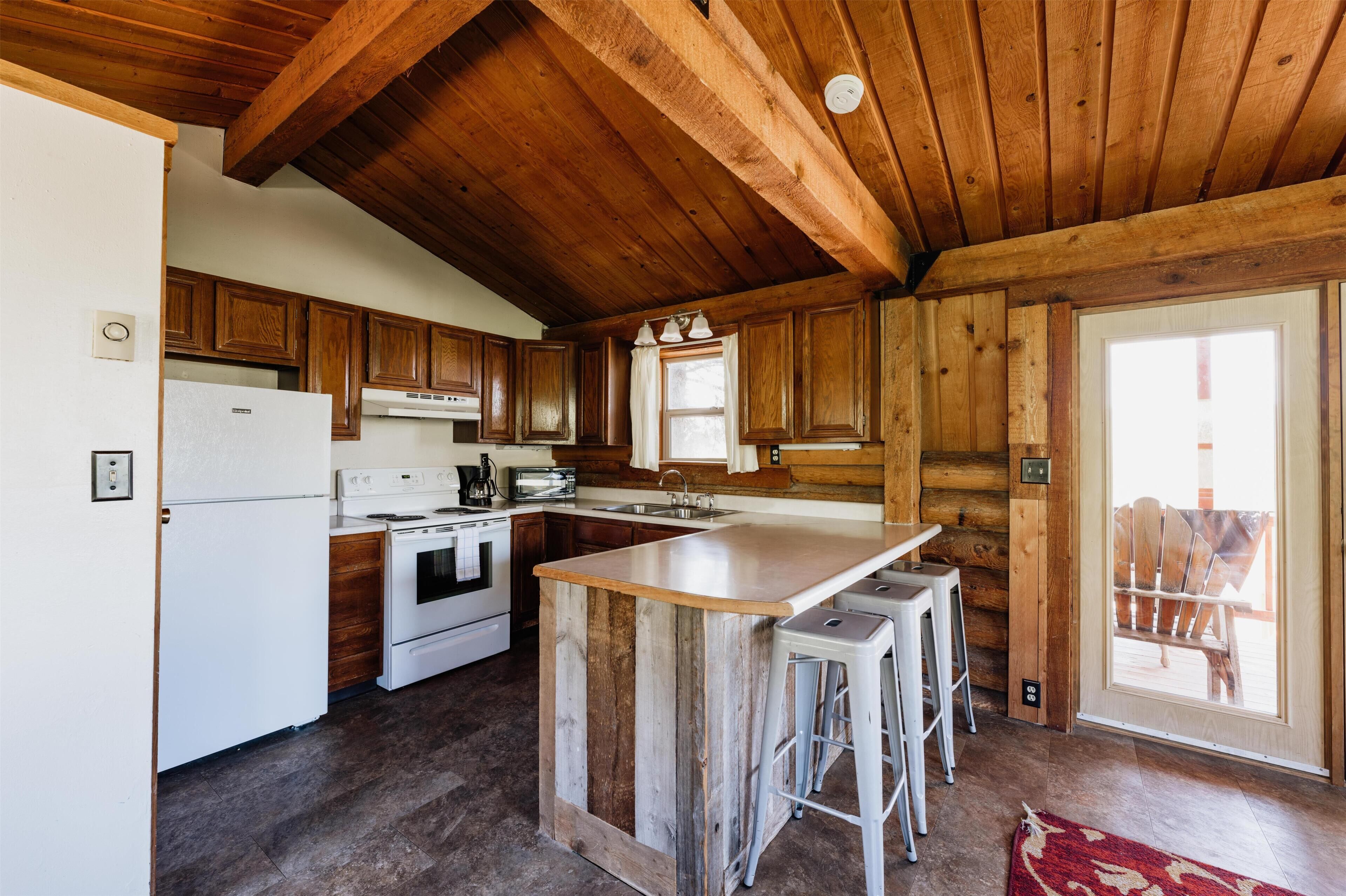 Una cocina rústica con armarios de madera, un refrigerador blanco, una estufa y una isla grande con taburetes de bar.