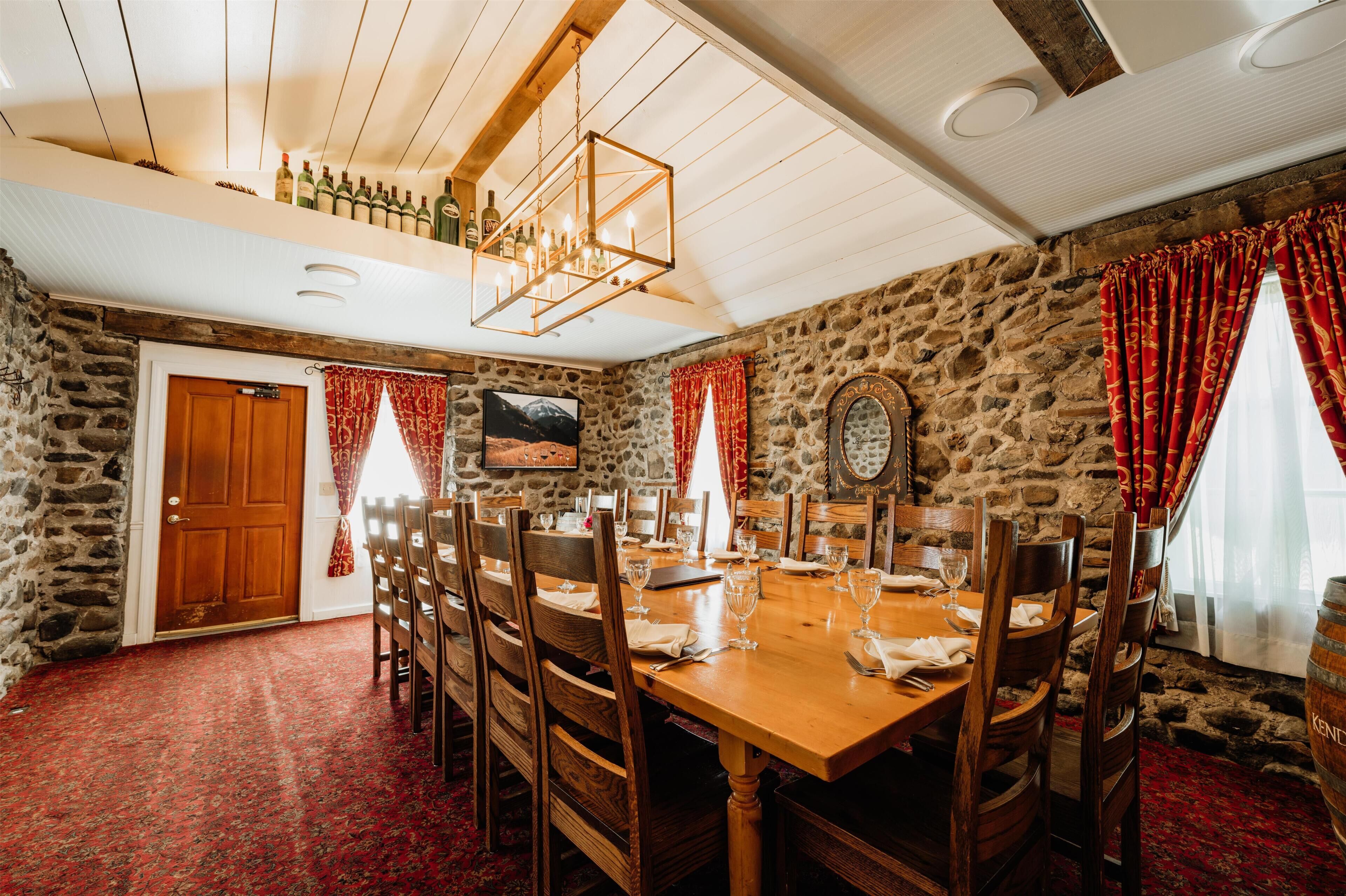 A dining room with a wooden table set for six, stone walls, and a chandelier.