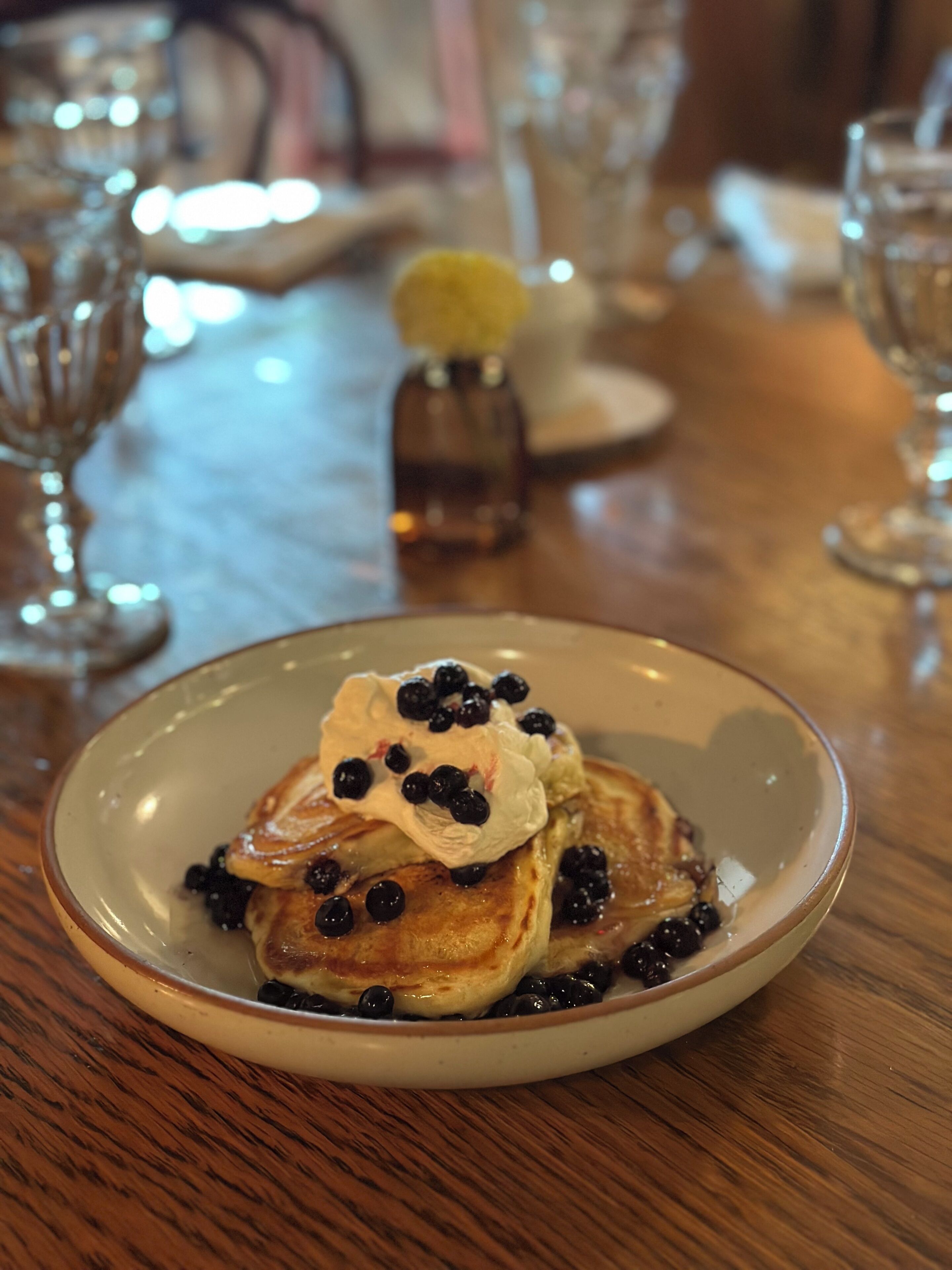 A plate of pancakes with blueberries and whipped cream on a wooden table.
