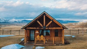 A wooden cabin with a porch, surrounded by a fenced area and snow patches, with mountains in the background. - Chico Hot Springs Resort & Day Spa (Pray)