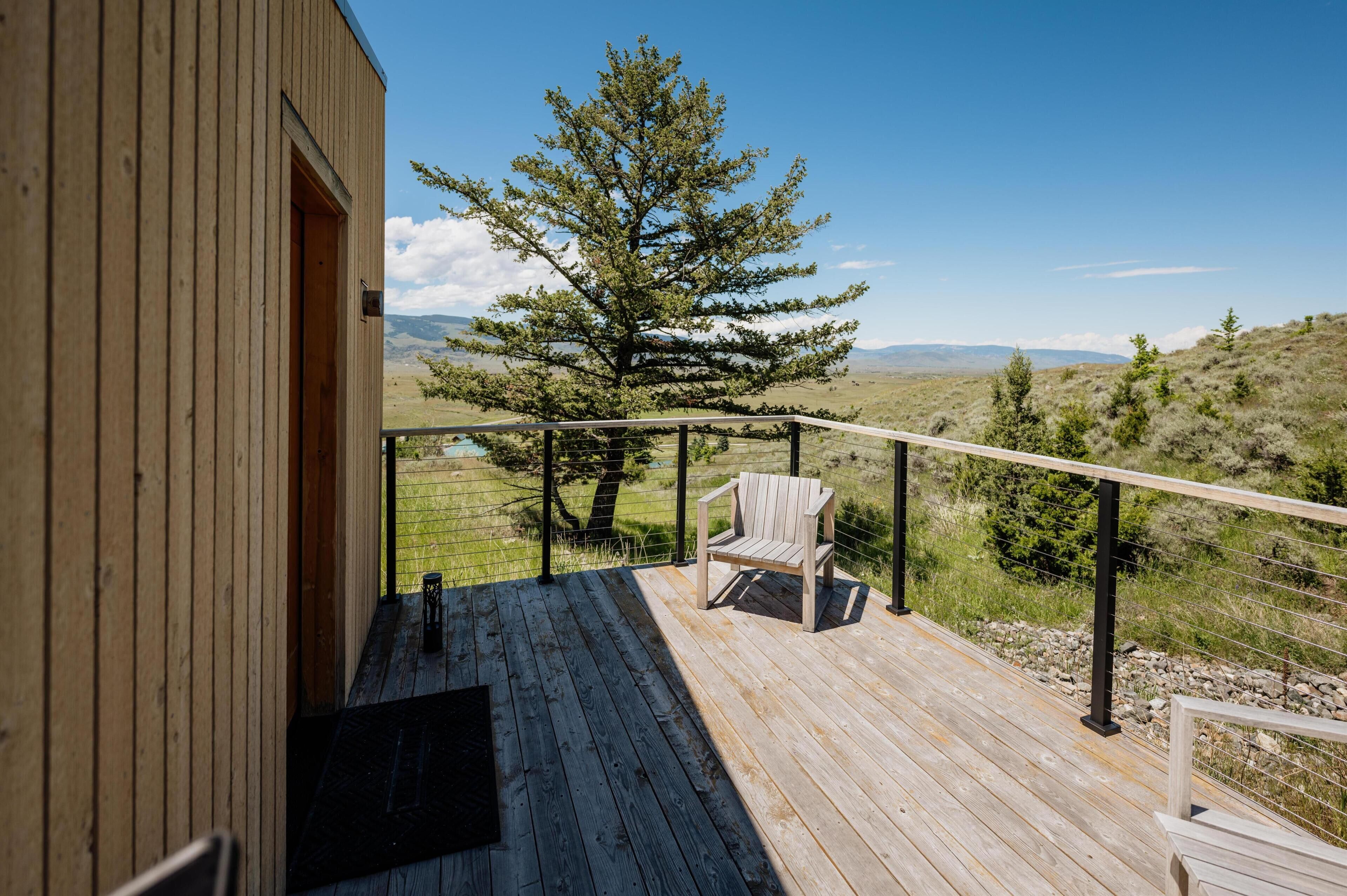 A wooden deck with a chair and a view of a tree and distant mountains.