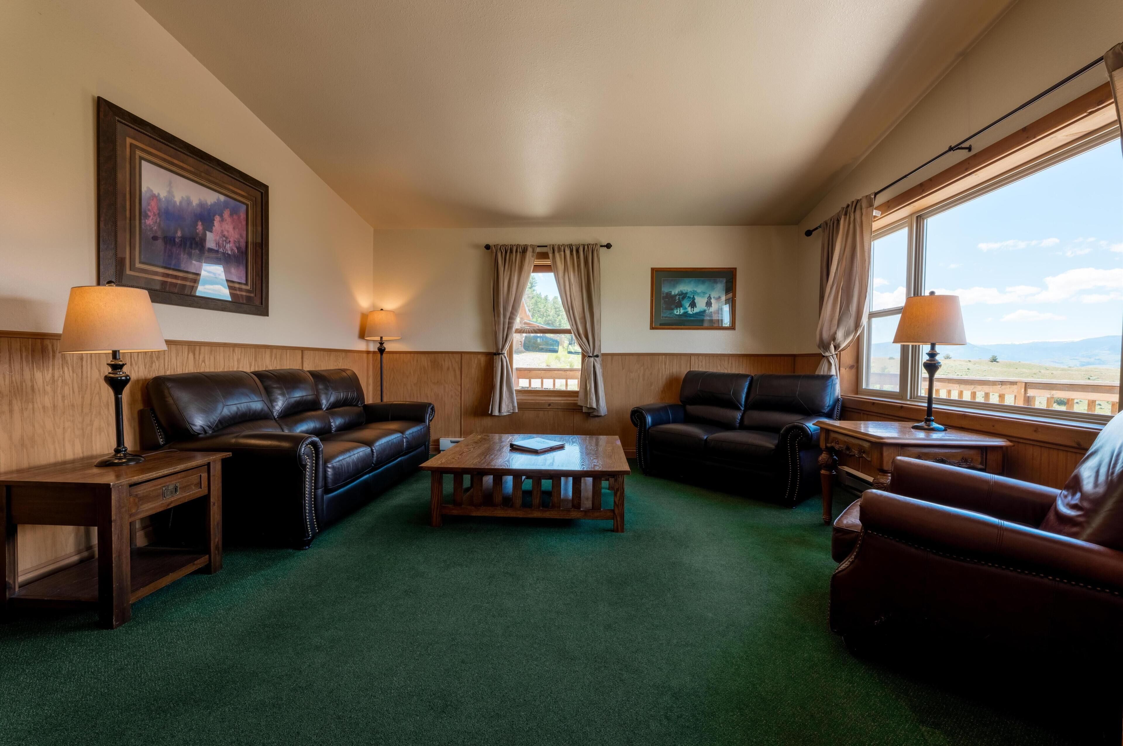 A room with a green carpet, two leather sofas, a wooden coffee table, and two lamps.