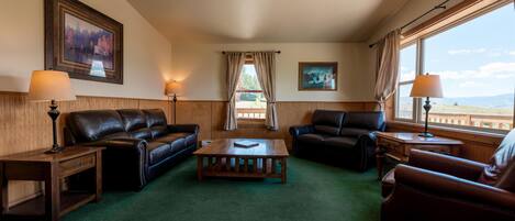 A room with a green carpet, two leather sofas, a wooden coffee table, and two lamps.