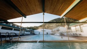 A swimming pool area with a wooden roof, a view of a building with 'HICO' signage, and a mountainous backdrop.