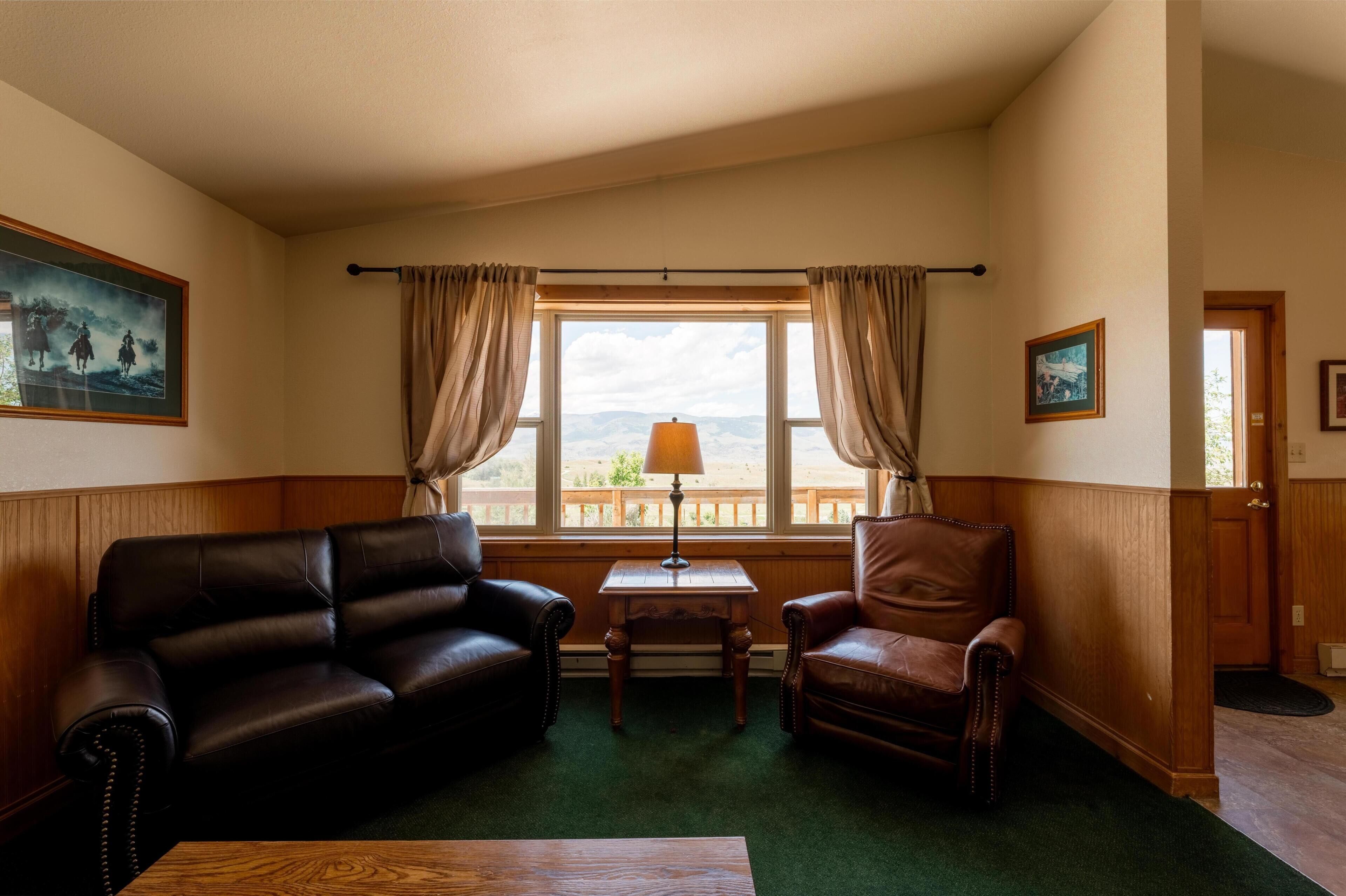A room with a large window, a wooden table, two leather sofas, and a lamp.