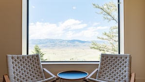 Two upholstered chairs facing a round table with a view of a mountainous landscape through a large window. - Chico Hot Springs Resort & Day Spa (Pray)