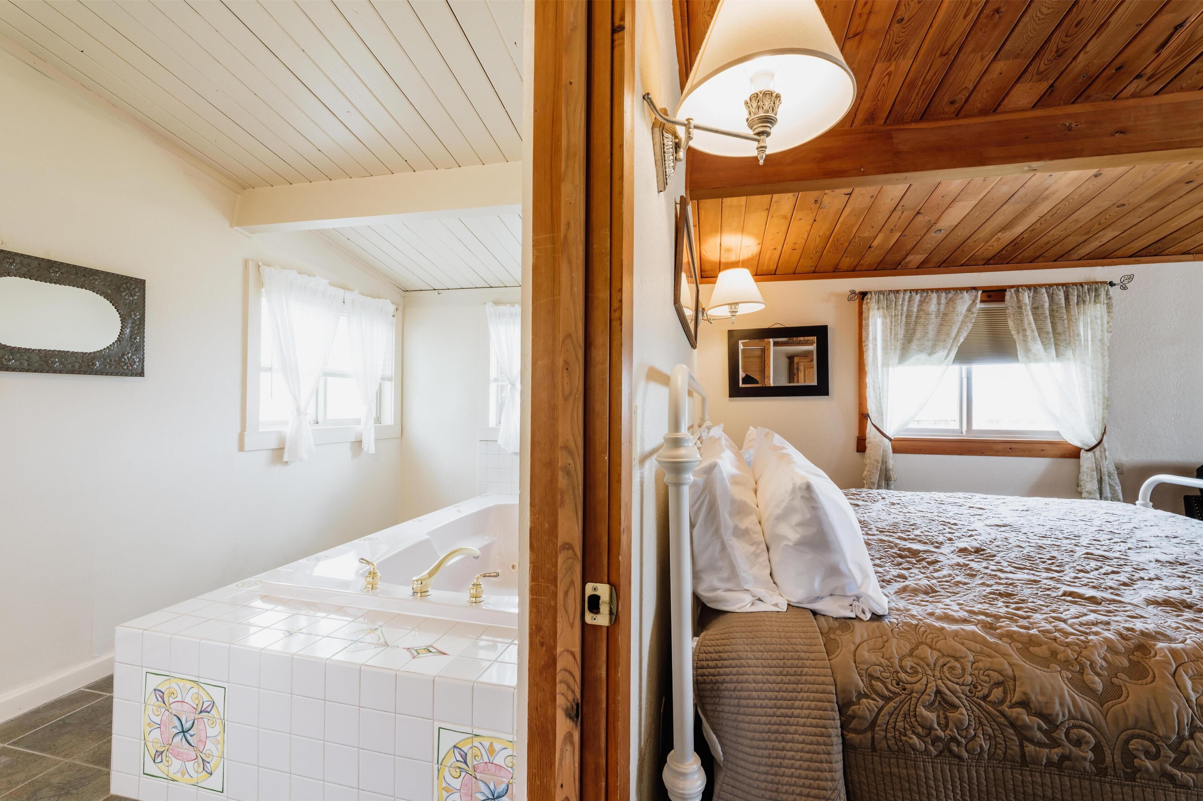 Une chambre à coucher avec un plafond en bois, un grand lit recouvert d’une courtepointe, une table de chevet et une fenêtre avec des rideaux.