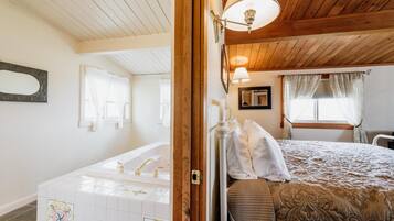 Une chambre à coucher avec un plafond en bois, un grand lit recouvert d’une courtepointe, une table de chevet et une fenêtre avec des rideaux.