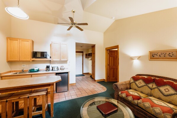 A compact kitchen with wooden cabinets, a microwave, and a refrigerator. There is a dining table with benches and a sofa in the living area. - Chico Hot Springs Resort & Day Spa (Pray)