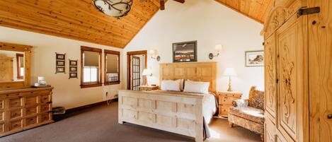 Un dormitorio amplio con una cama grande, techo de madera y un armario de madera.