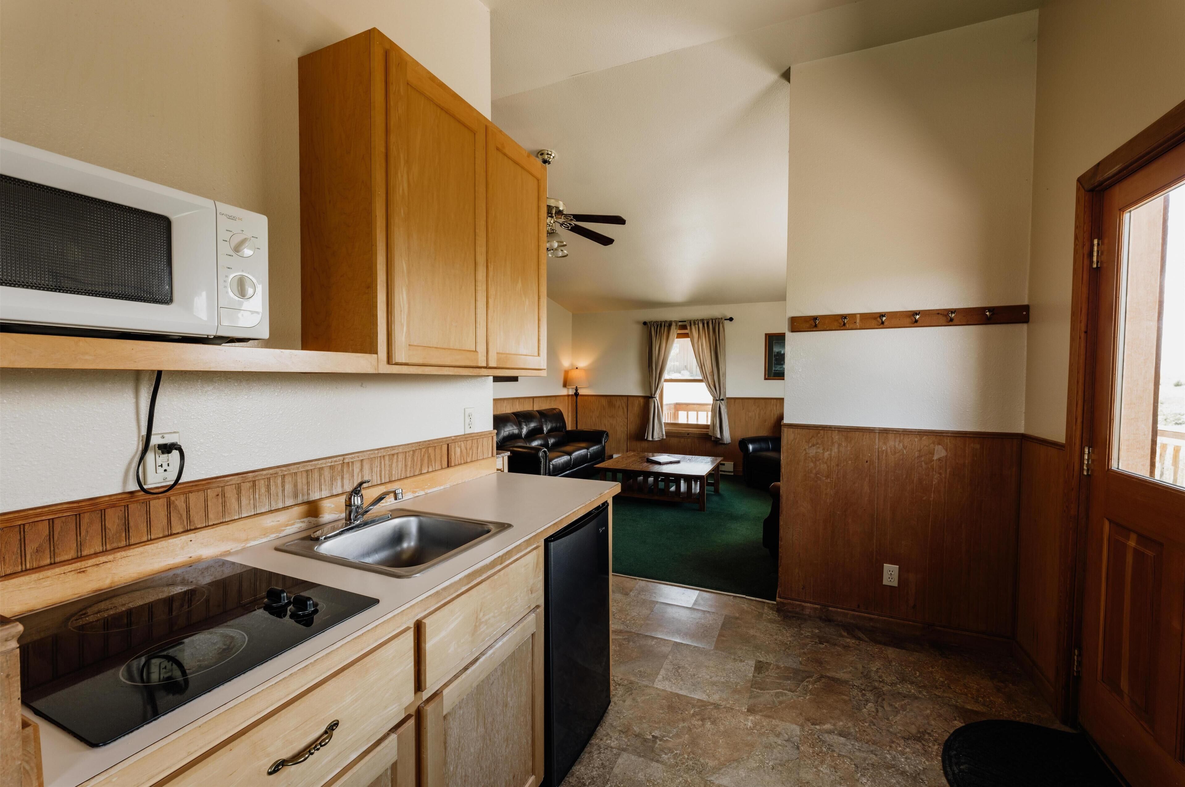 A compact kitchen with wooden cabinets, a microwave, a sink, and a dishwasher.