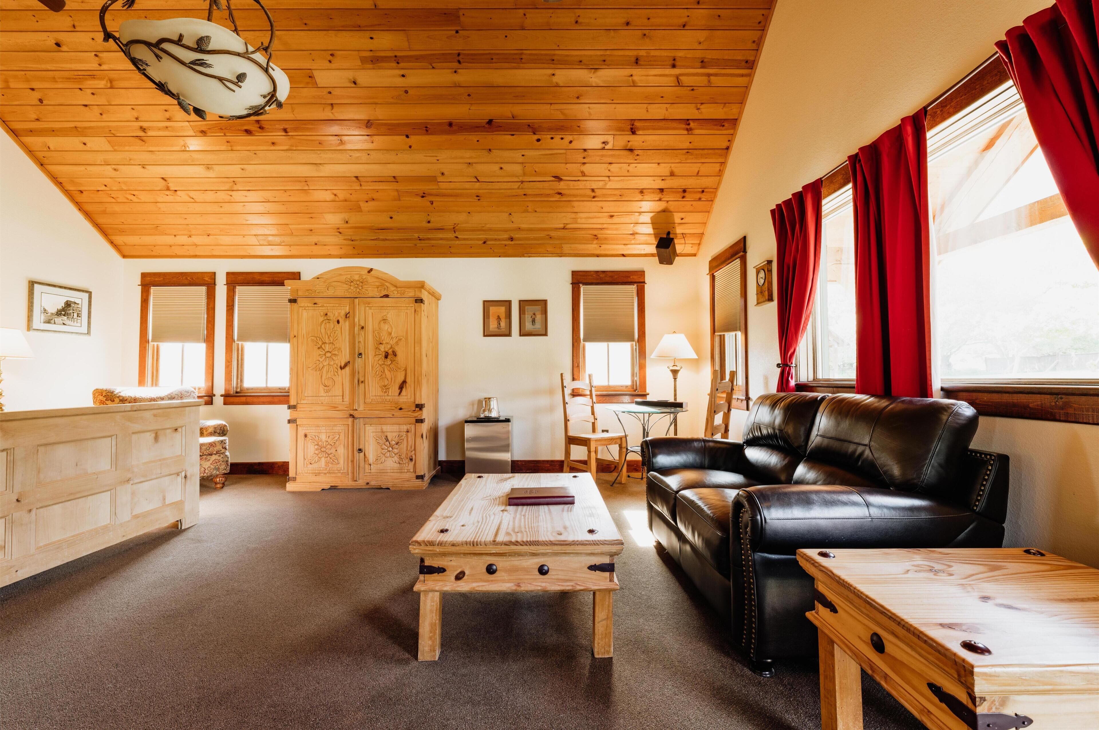 A cozy living room with a wooden ceiling, a leather sofa, a wooden coffee table, and a cabinet.