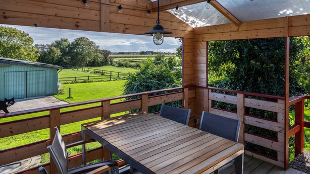 Una terraza de madera con una mesa y sillas, una lámpara colgante y vistas a un paisaje verde.
