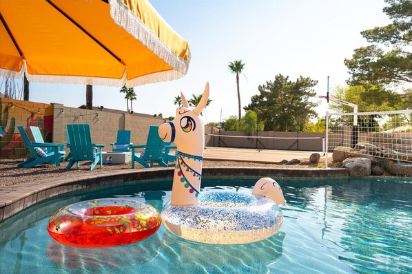 Une piscine avec des jouets gonflables, un parasol jaune et des chaises vertes.