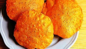 Three round, golden-brown fried items on a white plate, with a small bowl of mixed vegetables in the background. - Ascot By Glitz Hotels (Mumbai)