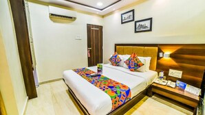 A hotel room with a bed, a bedside table, an air conditioning unit, and two framed pictures on the wall. - Ascot By Glitz Hotels (Mumbai)