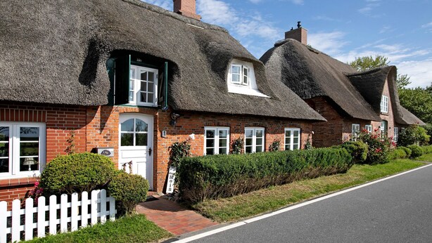 A row of thatched-roof cottages with brick walls, white windows, and a white picket fence. - Holiday Home 'Pellworm-Kate' with Private Terrace, Private Garden and Wi-Fi (Pellworm)