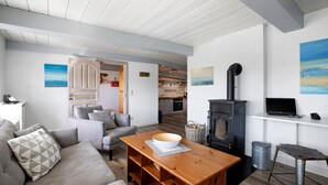 A modern living room with a sofa, a wooden coffee table, a fireplace, and a kitchen in the background. - Holiday Home 'Pellworm-Kate' with Private Terrace, Private Garden and Wi-Fi (Pellworm)