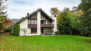 Une maison à deux étages avec un balcon, une pelouse et une clôture en bois.