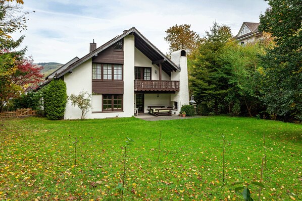 A two-story house with a balcony, a lawn, and a wooden fence.