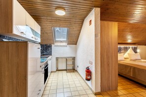 A compact hotel room with a kitchenette, a bed, a fire extinguisher, and a window.