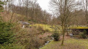 Un paysage rural avec une petite maison, un ruisseau et des arbres denses.