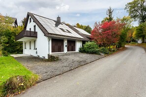 A single-story house with a sloped roof, a front porch, and a driveway leading to a road.