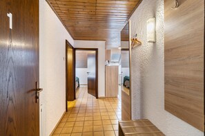 A hallway with wooden doors, a tiled floor, a wooden ceiling, and a light fixture on the wall.