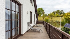 Een balkon met twee ligbedden, een houten vloer en uitzicht op een groen landschap.