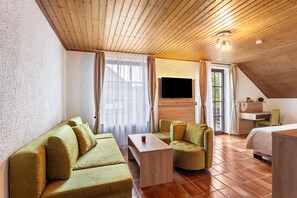 A room with a wooden ceiling, a flat-screen TV mounted on the wall, a sofa, a small table, and a bed.