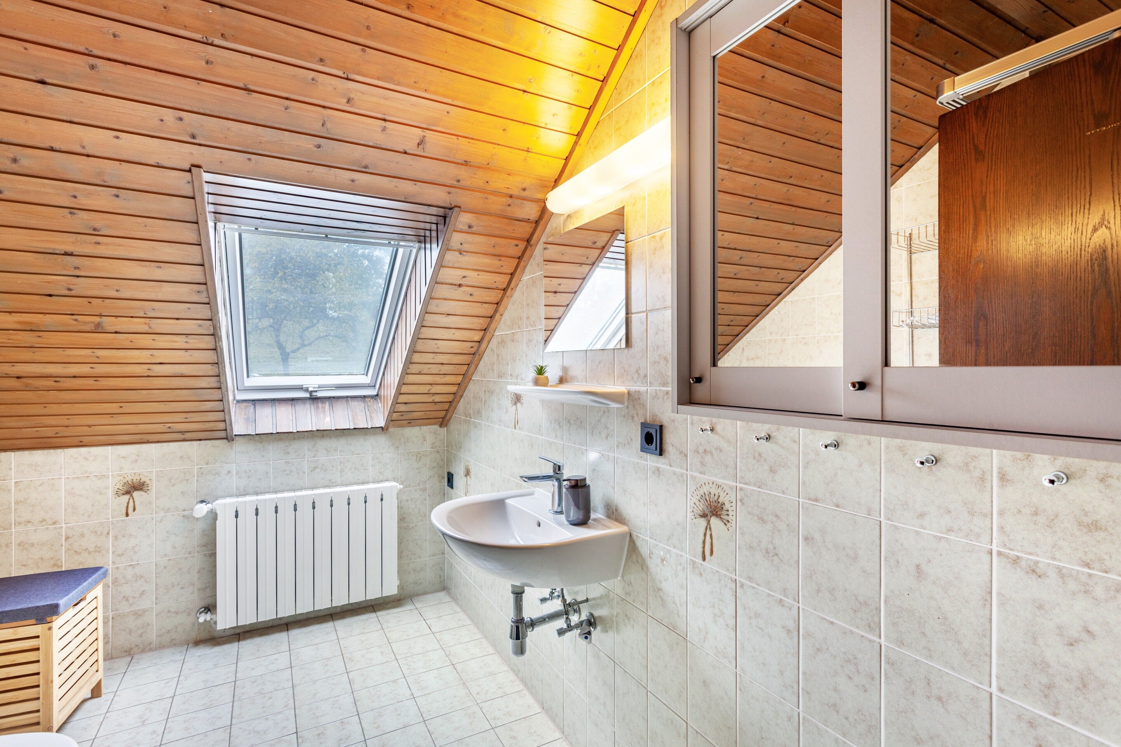 A modern bathroom with a wooden ceiling, a skylight, a white sink, and a large mirror.