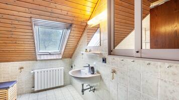 A modern bathroom with a wooden ceiling, a skylight, a white sink, and a large mirror.