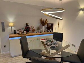 A modern dining area with a glass table, black chairs, a wooden counter, and holiday decorations. - Apartment 'Harzfewo Köhnke 1' with Mountain View, Shared Garden and Wi-Fi (Goslar)