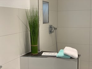 A bathroom with a shower, a towel rack, and a vase of green plants.