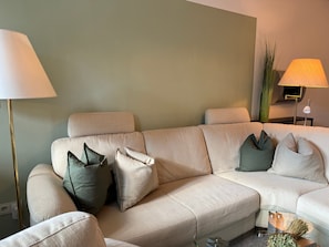 Un canapé beige agrémenté de plusieurs coussins, un lampadaire, une table d’appoint avec une lampe et un vase contenant des plantes séchées.