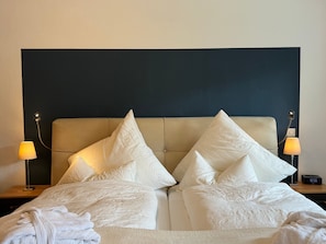 Un lit bien fait, avec du linge de lit blanc et des oreillers, une tête de lit sombre et des lampes de chevet.