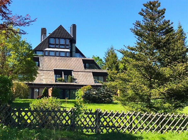 Une maison moderne avec un toit en pente, de grandes fenêtres et une cour clôturée.
