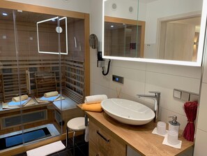 Un baño moderno con ducha envuelta en vidrio, un espejo grande, tocador de madera y calefacción integrada.