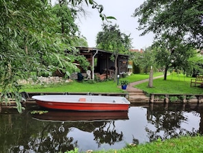 Un bateau était amarré dans une étendue d’eau calme, entourée de verdure et d’une petite construction en bois dotée d’un espace extérieur aménagé pour s’asseoir.