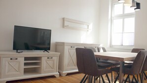 Moderni keittiö, jossa on televisio, puukalusteet ja ruokapöytä tuoleineen.