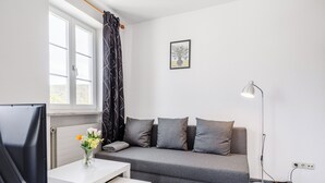 A modern living room with a grey sofa, a white table, a floor lamp, and a window with curtains. - Central charming apartment in the heart of Kulmbach (Kulmbach)