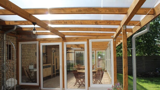 A covered patio with wooden beams and glass doors leading to an outdoor dining area. - Apartment 'Ferienwohnung Dg Rechts - Lychen' with Lake View, Shared Terrace and Wi-Fi (Lychen)